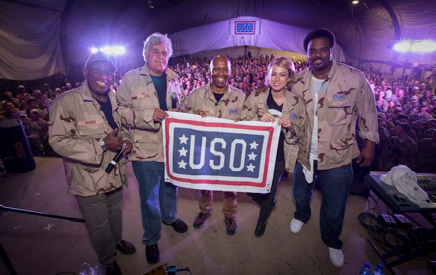 TODAY co-host Al Roker (l), comedian/entertainer legend (2nd l) , and musician Kevin Eubanks (c) along with comedians Iliza Shlesinger (2nd r) and Craig Robinson (r) proudly hold the USO flag on stage at the conclusion of the TODAY/USO Comedy Tour performance at Bagram Air Base in Afghanistan on October 1, 2014. (USO photo by Fred Greaves)